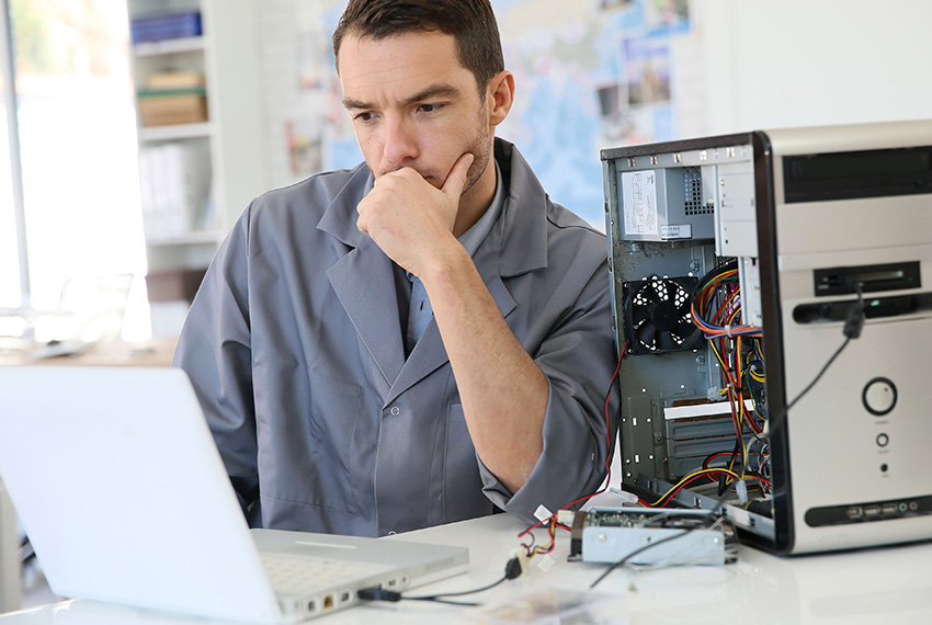 Technician in gray coat analyzing laptop performance with open desktop computer, emphasizing system tune-up services for optimal computer maintenance.