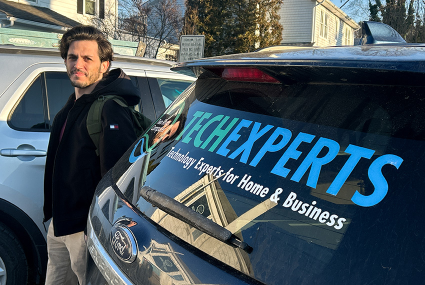 Man standing beside a vehicle with "TECH EXPERTS" branding, showcasing services for home and business, emphasizing on-site IT support.
