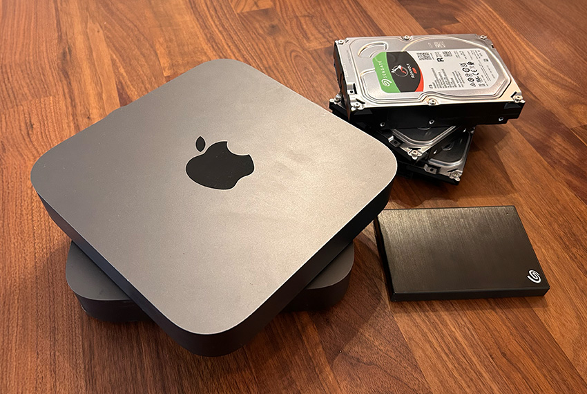 Apple Mac mini with external hard drives and SSD on wooden surface, representing data recovery solutions and storage options.